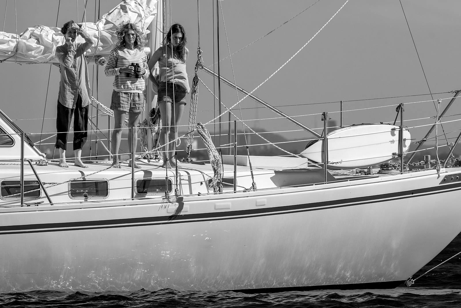 Three women standing on a sailboat deck in black and white